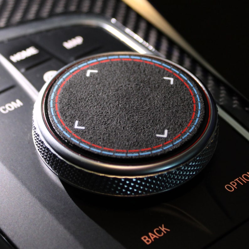 May include: Close-up of a black and silver car control knob with a textured surface and four white directional arrows. The knob has a red and blue ring around the edge.