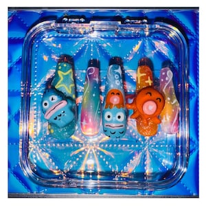 May include: A set of five colorful fake nails with a cartoon character design. The nails feature a blue and green character with a pink mouth, a blue and green character with a pink mouth and a white eye, a blue and green character with a pink mouth and a white eye, an orange character with a pink mouth and a white eye, and a blue and green character with a pink mouth and a white eye.