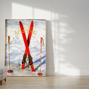 K&ouml;nnte beinhalten: Ein Vintage-Skiposter mit einem Paar roter Ski, die &uuml;bereinander gekreuzt sind, mit braunen Skischuhen und zwei Holzskist&ouml;cken. Das Poster hat einen wei&szlig;en Hintergrund mit einer verschneiten Landschaft und den Text "APRES SKI" in goldenen Buchstaben.