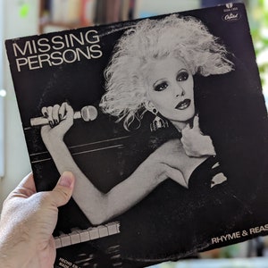 May include: Black and white album cover for Missing Persons, featuring a woman with voluminous blonde hair holding a microphone. The album title "Missing Persons" is at the top, with "Rhyme & Reason" at the bottom. The Capitol Records logo is visible.