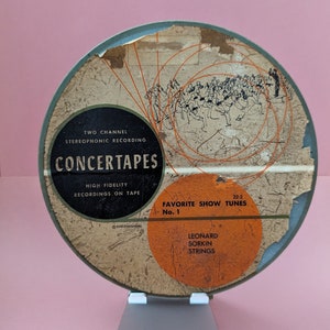May include: A vintage green and orange reel-to-reel tape with the text "CONCERTAPES" and "FAVORITE SHOW TUNES No. 1 LEONARD SORKIN STRINGS" on the label.