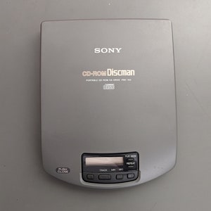 May include: A gray Sony CD-ROM Discman PRD-160 portable CD-ROM XA drive with a black button labeled "PUSH CLOSE" and a display screen with "TRACK", "MIN", and "SEC" labels.