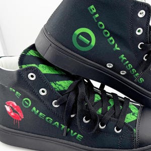 May include: Black high-top sneakers with green and white graphic designs and text. The sneakers feature black laces, soles, and toe caps. The text includes "BLOODY KISSES" and "TYPE O NEGATIVE". A red lip graphic is also visible.