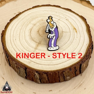 Puede incluir: Un pin de dibujos animados con un personaje con una t&uacute;nica morada con ribetes blancos, sosteniendo un cetro dorado. El pin est&aacute; etiquetado "Kinger - Style 2" en texto rojo. El pin est&aacute; sobre una rodaja de madera.