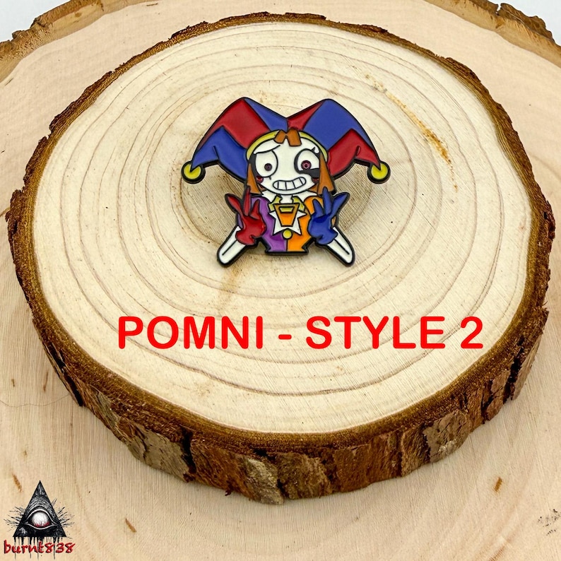 Puede incluir: Un colorido pin de esmalte con un personaje de buf&oacute;n de dibujos animados con un sombrero rojo, azul y amarillo. El buf&oacute;n tiene una cara blanca, un contorno negro y viste un atuendo morado, naranja y amarillo. El texto "POMNI - STYLE 2" est&aacute; en rojo.