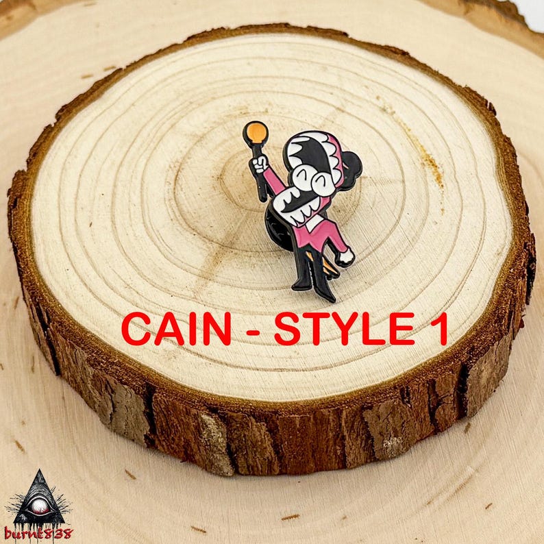 Puede incluir: Un colorido pin de esmalte con un personaje de dibujos animados con un atuendo rosa, sosteniendo un objeto dorado. El pin tiene detalles en negro y el texto "CAIN - STYLE 1" en rojo. El pin est&aacute; sobre una rodaja de madera.
