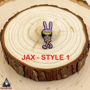 Puede incluir: Un pin de conejo morado con una sonrisa amarilla y un peto rosa. El pin est&aacute; sobre una rodaja de madera con el texto "JAX - STYLE 1". El personaje de dibujos animados tiene zapatos negros y una mochila negra.