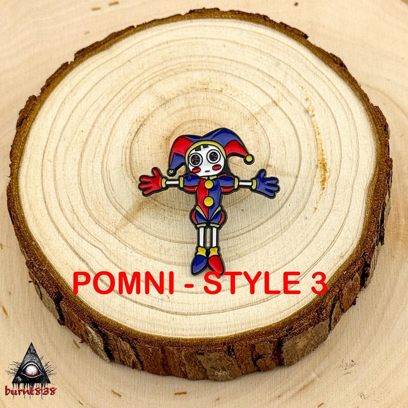 Puede incluir: Un pin de esmalte colorido con un dise&ntilde;o de buf&oacute;n con acentos rojos, azules y amarillos. El pin tiene los brazos extendidos y est&aacute; sobre un fondo de madera. Se muestra el texto "POMNI - STYLE 3".