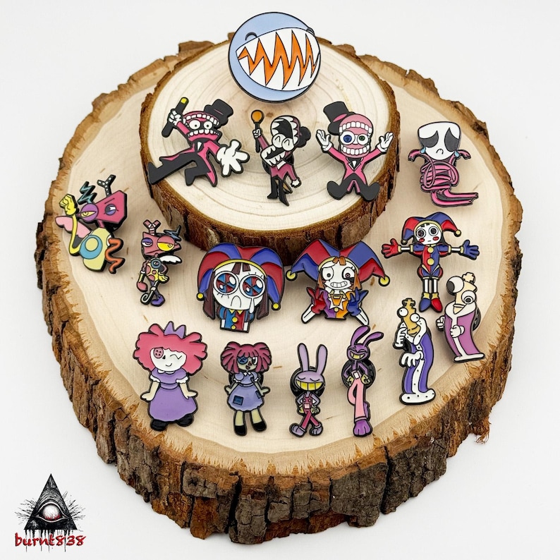 Puede incluir: Una colecci&oacute;n de coloridos pines de esmalte con varios personajes de dibujos animados con dise&ntilde;os &uacute;nicos. Los pines incluyen personajes con sombreros de copa, sombreros de buf&oacute;n y otros elementos caprichosos. Los pines se exhiben sobre una rodaja de madera.