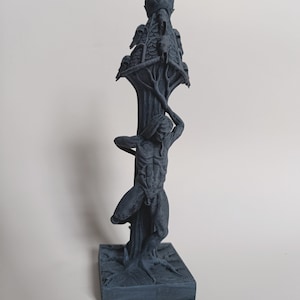 May include: A dark grey 3D printed sculpture of a figure climbing a tree with a skull-shaped structure at the top.