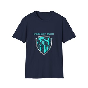 May include: Navy blue t-shirt with a teal and silver shield design featuring a circuit board pattern. The text "CYBERSECURITY ANALYST" is above the shield. A casual tee for tech professionals.
