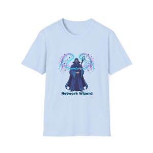 May include: Pale blue t-shirt with a graphic of a robed wizard holding a staff, with swirling energy effects in blue, purple, and teal. The text "Network Wizard" is printed below the graphic. The shirt is a short-sleeved crew neck.