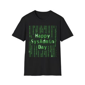 Op de afbeelding: Zwart t-shirt met een groene afbeelding met de tekst "Happy SysAdmin Day". De afbeelding toont een matrix van groene binaire code. Het t-shirt is gemaakt van een zacht materiaal.