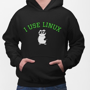 May include: A black hooded sweatshirt featuring a graphic of a white penguin wearing black sunglasses. Above the penguin, the text "I USE LINUX" is printed in a bright green font. The hoodie includes a front kangaroo pocket and long sleeves.