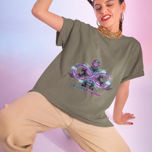 Puede incluir: Una camiseta de color verde oliva con un estampado gráfico de un personaje futurista con traje oscuro y un símbolo de infinito de color púrpura brillante. El texto "DevOps Engineer" aparece impreso en una fuente estilizada bajo el personaje, en tonos púrpuras y azules.