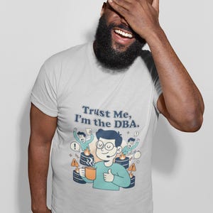 Könnte beinhalten: Ein hellgraues Kurzarm-T-Shirt mit einer grafischen Illustration einer Person mit Headset, die eine Tasse hält, umgeben von brennenden Servern und panischen Kollegen, mit dem Text "Trust Me, I'm the DBA." in Dunkelblau.