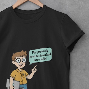 Könnte beinhalten: Ein schwarzes Kurzarm-T-Shirt mit einer Cartoon-Illustration einer Person mit Brille, die einen Laptop hält und auf eine hellgrüne Sprechblase zeigt, die den Text enthält, You probably need to download more RAM.