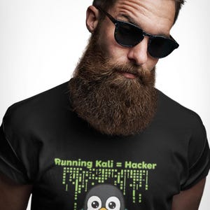 Puede incluir: Una camiseta negra con un gráfico de un pingüino con una sudadera con capucha de color verde azulado. Sobre el pingüino, el texto Running Kali = Hacker aparece en verde claro. El diseño incluye un patrón digital tipo matriz en verde.