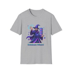 Op de afbeelding: Grijs t-shirt met een kleurrijke illustratie van een tovenaar in een paarse jurk en hoed, met een baard, die een stapel blauwe en paarse datacilinders vasthoudt. De tekst "Database Wizard" staat eronder.