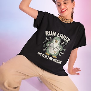 Pode incluir: Uma t-shirt preta com um gráfico de um pinguim a segurar um documento rasgado com as etiquetas Software Agreement e Invoice. O texto acima do pinguim diz RUN LINUX e o texto abaixo diz NEVER PAY AGAIN, rodeado por ícones de cadeados.