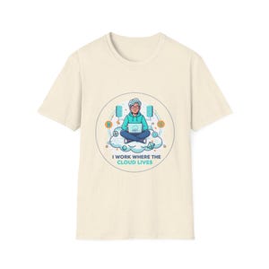 Peut inclure: T-shirt crème avec un motif circulaire représentant une personne assise sur un nuage, utilisant un ordinateur portable. Le motif comprend des icônes de serveur et le texte "I WORK WHERE THE CLOUD LIVES" en turquoise.