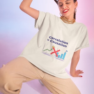 May include: A cream-colored short-sleeve t-shirt featuring a graphic print with the text "Correlation = Causation" above a line graph showing an upward trend and a bar chart with a red "X" mark crossing out the connection between the two.