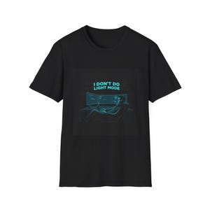 Pode incluir: T-shirt preta com um gráfico turquesa. O gráfico mostra uma pessoa relaxando em frente a dois monitores de computador, com o texto "I DON'T DO LIGHT MODE" acima. A pessoa está segurando uma bebida.