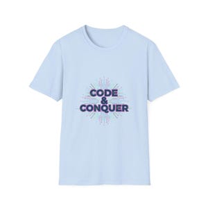 Könnte beinhalten: Hellblaues T-Shirt mit dem Schriftzug "CODE & CONQUER" in einer stilisierten Schriftart. Der Text ist von einem Leiterplattendesign in Blau-, Lila- und Grüntönen umgeben.