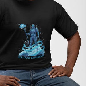 May include: A black t-shirt featuring a graphic print of a futuristic figure in blue armor holding a staff with a glowing cloud icon. The figure stands on stylized blue clouds and digital lines. The text CLOUD ENGINEER is printed in blue below.