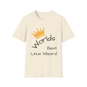 May include: A cream-coloured t-shirt featuring the text "Worlds Best Linux Wizard" in black, with a gold crown graphic. The short-sleeved, crew neck shirt is designed for casual wear. The design is printed on the front of the shirt.