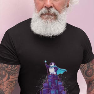 May include: A black short-sleeved t-shirt featuring a graphic of a penguin wearing a blue cape and holding a staff while standing atop a stack of purple server towers. The text "LINUX LEGEND" is printed in light blue letters at the bottom.