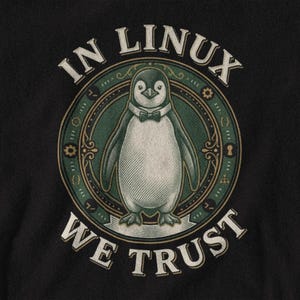 May include: A black t-shirt featuring a circular graphic with a central penguin wearing a bow tie. The design includes the text IN LINUX WE TRUST in a cream-colored serif font, surrounded by green and gold decorative elements and icons.