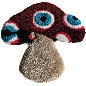 May include: A plush mushroom-shaped rug with a red cap and a brown stem. The cap has three large, colorful eyes with white, red, and blue details.