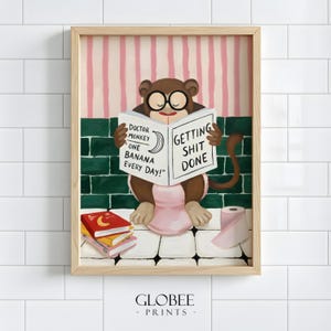 May include: A framed print depicting a cartoon monkey wearing glasses, reading a book with the text "Getting Shit Done." The book also reads "Doctor Monkey One Banana Every Day!" A roll of toilet paper and books are also visible.