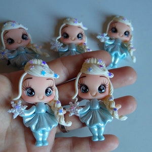 K&ouml;nnte beinhalten: Eine Sammlung von f&uuml;nf Miniaturfiguren. Jede Figur hat ein hellblaues Kleid, blondes Haar und eine sternf&ouml;rmige Krone. Die Figuren halten schneeflockenf&ouml;rmige Objekte. Die Gesichter haben gro&szlig;e, ausdrucksstarke Augen.