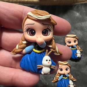 May include: Handmade polymer clay figurines of a princess in a blue dress with brown hair and a white headband. Each figurine has a small snowman companion. The figures are detailed with painted facial features and are approximately 2 inches tall.