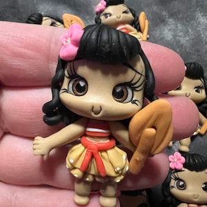May include: A collection of small, handcrafted figurines. Each figurine features a cartoon character with dark hair, a pink flower, and a yellow skirt with white polka dots. The character is holding a tan object.