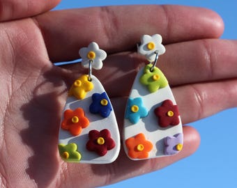May include: A pair of white teardrop-shaped earrings with colorful flower accents. The earrings have a white background with yellow, orange, red, green, blue, and purple flowers.