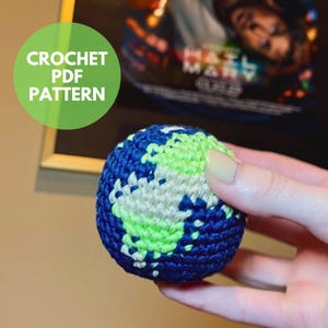 May include: A crocheted globe in blue, green, and cream colors. The continents are green and cream, while the oceans are blue. The text "CROCHET PDF PATTERN" is in a green circle.