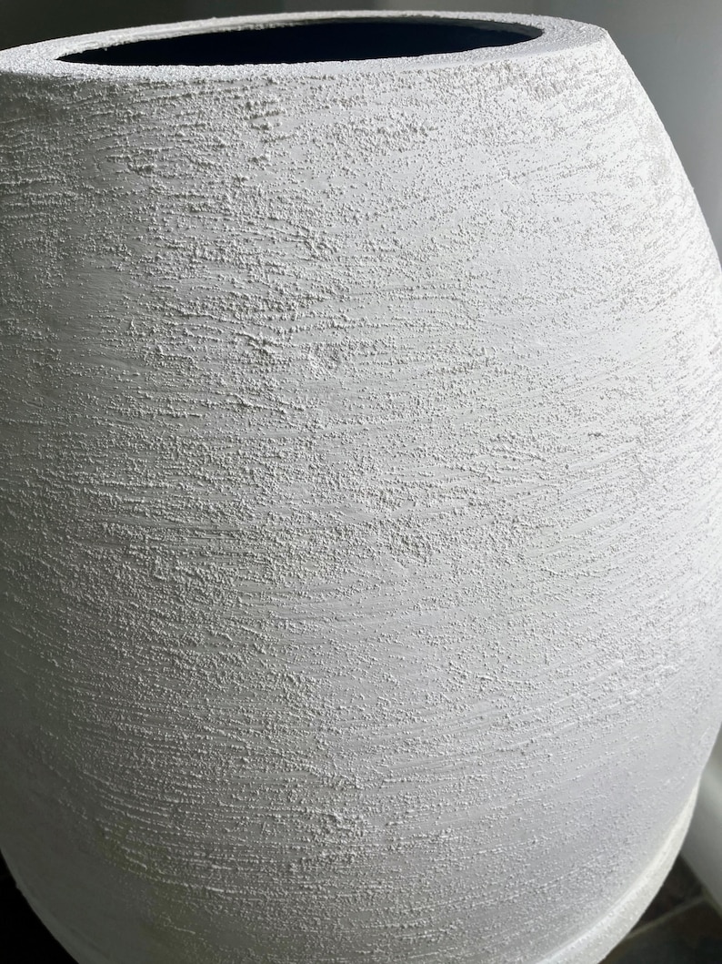 Pode incluir: Um vaso de cer&acirc;mica branco com uma superf&iacute;cie texturizada. O vaso tem uma forma arredondada e uma abertura larga.