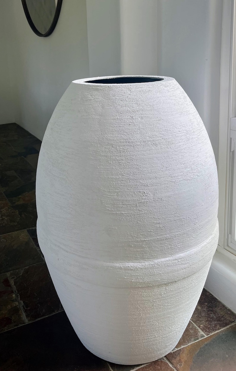 Pode incluir: Um vaso grande de cer&acirc;mica branca texturizada com formato arredondado. O vaso tem uma borda preta lisa.