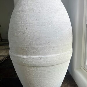 Pode incluir: Um vaso grande, branco, de forma oval e com superf&iacute;cie texturizada. O vaso tem uma faixa ligeiramente elevada ao redor do meio.