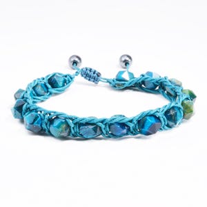 May include: A turquoise beaded bracelet with a macrame design. The bracelet features faceted, blue-green gemstones and adjustable sliding knots. The ends have small, silver-colored beads.