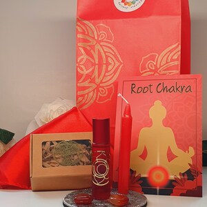 Puede incluir: Una bolsa de regalo roja con un diseño de mandala dorado, una vela roja, una botella de aceite esencial roja con un símbolo de chakra dorado, una pequeña caja con un diseño de árbol dorado y una tarjeta que dice "Root Chakra" con un símbolo de chakra rojo y una silueta de una persona en una postura de yoga.