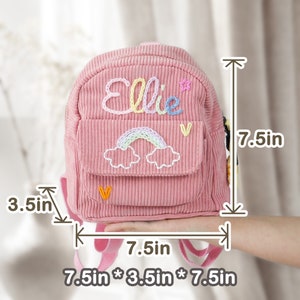 May include: Pink corduroy mini backpack with a rainbow and cloud embroidery and the name "Ellie" embroidered on the front. The backpack measures 7.5 inches tall, 7.5 inches wide, and 3.5 inches deep.