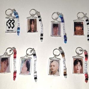 May include: A collection of eight keychains. Each keychain has a clear rectangular pendant with a photo of a person or a logo. The keychains are attached to a silver ring and a beaded strand with a name.