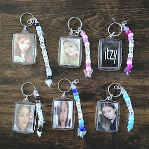 May include: Seven clear plastic keychains with colorful beaded chains. Each keychain features a photo of a different member of the K-pop group ITZY. The beads on the chains spell out the names of each member: Chaeryeong, Yuna, Ryujin, Lia, and Itzy.