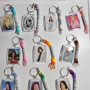 May include: A set of 10 keychains with clear plastic frames and colorful beaded charms. Each keychain features a different photo of a female K-pop idol. The charms spell out the names of the idols:  Eunjung, After School, Playgirlz, Uee, Nana, Kahi, Jungah, Bekah, Raine, and Jooyeon.