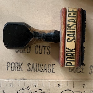 Puede incluir: Un sello de madera con un marco rojo y blanco y el texto "PORK SAUSAGE" en letras negras. El sello se utiliza para marcar productos c&aacute;rnicos.