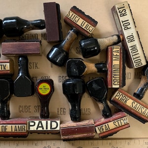 Puede incluir: Una colecci&oacute;n de sellos de madera y goma vintage con varias etiquetas, incluyendo "Ground Meat", "Bottom Rd. Pot Rst", "Pork Sausage", "Paid", "Breast of Lamb" y "Veal Stew".